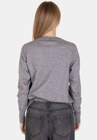 Maglione grigio con scollatura rotonda e maniche lunghe, abbinato a jeans neri a vita alta. Tessuto morbido, vestibilità casual.