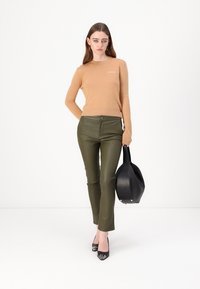 Tan knitted sweater with ribbed cuffs, paired with olive green leather pants and black handbag. Model wears black open-toe heels.
