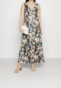 Pitkä hihaton mekko syvällä V-pääntiellä, jossa on värikäs abstrakti kuvio. Mukana pieni vaalea clutch-laukku ja nauhakengät.