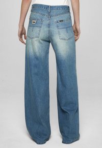 Modre hlače širokih nog z jeansa, z bledim učinkom, dvema žepoma na hrbtni strani z detajli šivov in značko z logotipom na desnem žepu.