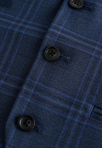 Marineblaue Stoff mit einem karierten Muster und hellblauen Linien, vier schwarzen Knöpfen und einer strukturierten Oberfläche.