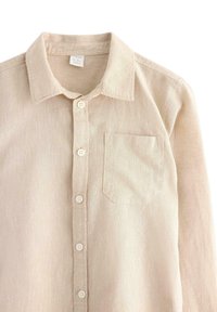 Camicia di lino beige chiaro con colletto, taschino sul petto e quattro bottoni lungo la parte anteriore. La trama è leggermente stropicciata e morbida.