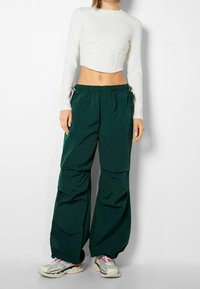 Vit ribbad långärmad croppad topp i kombination med lösa, mörkgrönaCargo-byxor med elastisk midja och sidfickor. Sneakers med flerfärgade accenter.