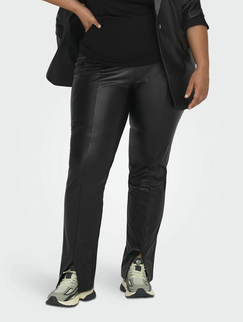 Zwarte faux leren broek met een slim fit, voorzien van zijslits bij de enkels. Gecombineerd met lichtgrijze sport schoenen.
