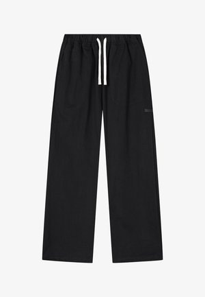 Pantaloni neri a vestibilità ampia con vita elastica e coulisse bianca, dotati di una piccola tasca laterale sulla gamba destra.