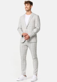 Costum gri deschis cu un model în carouri, sacou cu un singur nasture, pantaloni pe măsură și tricou alb, completat de adidași albi.