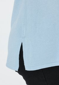 Hellblauer Pullover mit einer weichen Textur, ausgestattet mit seitlichen Schlitzen und einem geraden Saum, kombiniert mit schwarzen Hosen.