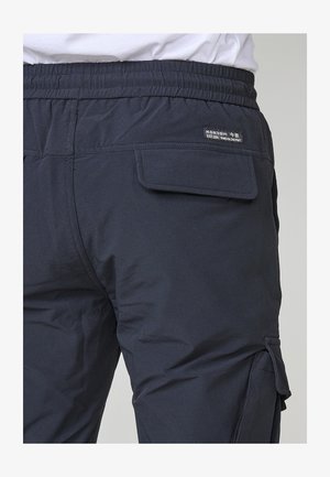 Sötét navy kargo nadrág rugalmas derékkal és egy oldalsó zsebbels. Az anyag sima textúrával rendelkezik, enyhén bordázott mintával.