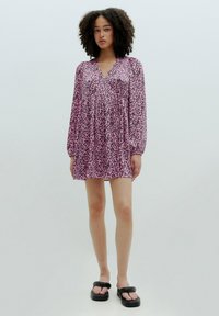 Rosa Kleid mit schwarzem Leopardenmuster, V-Ausschnitt, langen Puffärmeln und gerafftem Taillenbereich. Tragen mit schwarzen Plateausandalen.