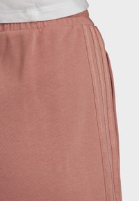 Rosa träningsbyxor gjorda av mjukt, strukturerat tyg. Har resårmidja och tre vertikala ränder längs sidan.