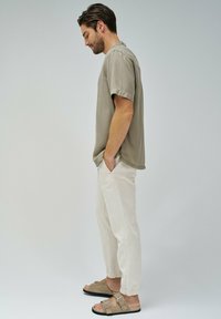 Camisa de manga corta gris claro, pantalones beige de corte relajado y sandalias marrones tipo slider. La camisa tiene cuello y un diseño sencillo.