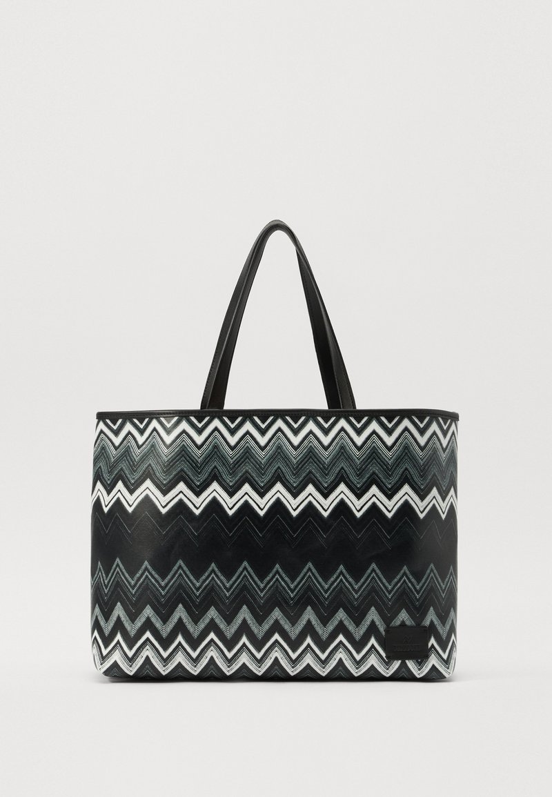 Tote bag in a black and white zigzag pattern, featuring smooth plastic material, two black handles, and a rectangular shape.