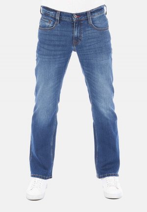 Jeans de mezclilla azul con un diseño de pierna recta, zonas deslavadas, estilo clásico de cinco bolsillos y cierre de botón. Llevados con sneakers blancos.
