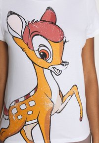 Vit t-shirt med en grafik av en tecknad hjort med orangea och rosa accenter, svarta konturer och en slitningseffekt på trycket.