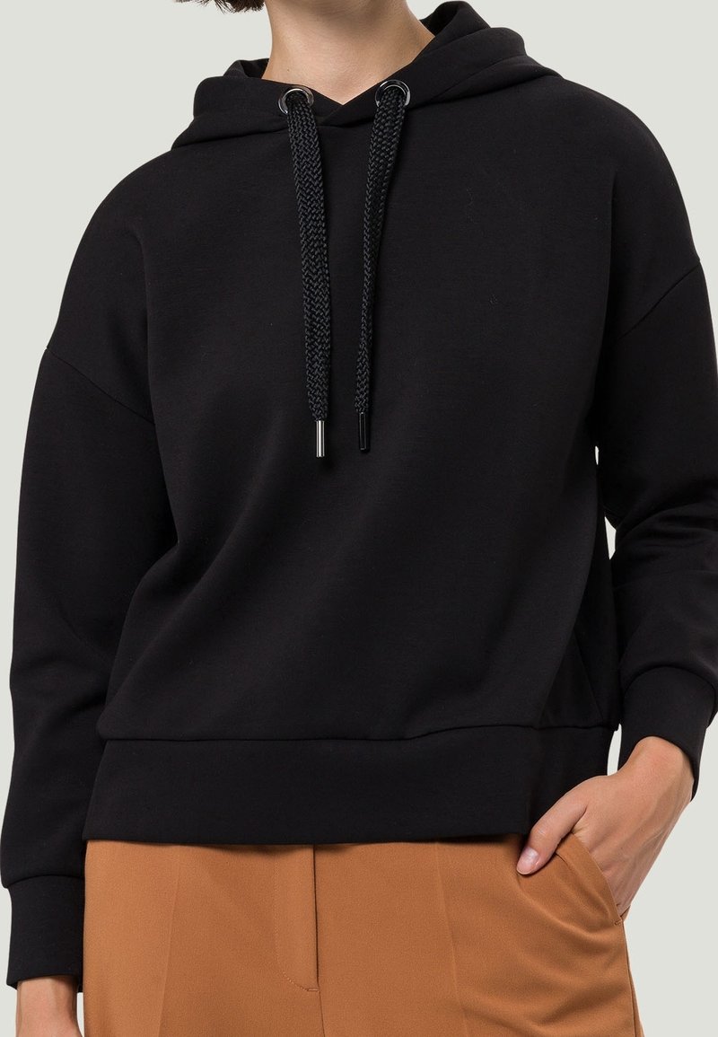 Zwarte katoenen hoodie met een ruime capuchon, gevlochten koordjes en geribde zoom. Heeft een ontspannen pasvorm en een zachte textuur.