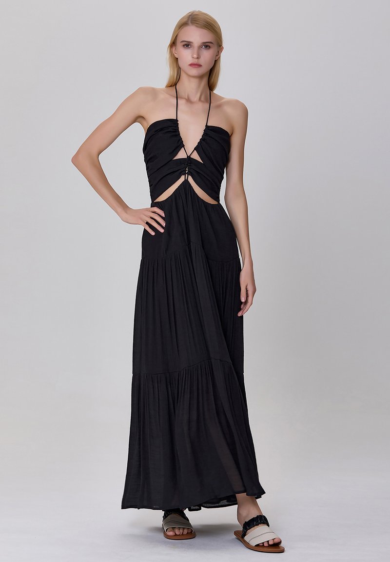 Robe maxi noire avec un col halter, un corsage froncé et des découpes. Tissu fluide avec des couches superposées, associée à des sandales plates.