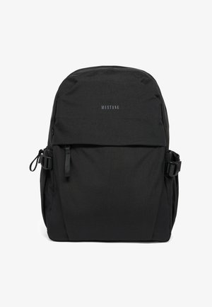 Black Mustang backpack with front zip pocket, side buckles, and minimalistic design, shown against a white background.