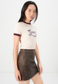 Kort beige crop-top med burgunder detaljer, med "Guess" logoen, kombinert med et brunt faux lær mini-skjørt.