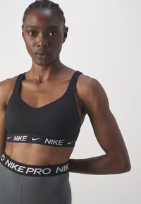 Svart sports-BH med scoop-hals og brede stropper. Har et merket elastisk bånd med "NIKE PRO" i hvite bokstaver.