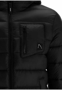 Sort pufferjakke med en lynlåslomme på brystet, stitched detaljer og et logo patch. Materialet er glat med en polstret tekstur.