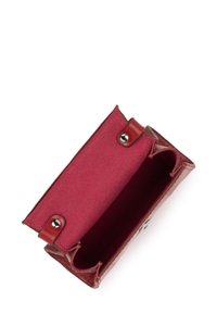 Piccola cintura in pelle rossa aperta, che mostra un interno in feltro e bottoni a pressione in metallo, isolata su sfondo bianco.