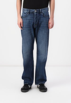 Jeans in denim blu con un design a gamba dritta, cinque tasche e chiusura con bottone. Indossati con sneakers nere.