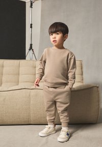 Hanorac bej și pantaloni de trening asortați cu croială conică, realizați dintr-un material moale, asortați cu adidași crem cu accente albastre și roșii.