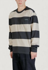 Camicia a maniche lunghe in cotone a righe nere e beige. Presenta una tasca sul petto sinistro con etichetta logo. Colletto e polsini a coste.