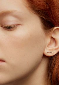Pendiente de oreja plateado con cinco pequeñas gemas transparentes, que presenta un diseño elegante y minimalista. La pieza abraza estrechamente el lóbulo de la oreja.
