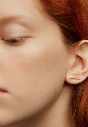 Pendiente de oreja plateado con cinco pequeñas gemas transparentes, que presenta un diseño elegante y minimalista. La pieza abraza estrechamente el lóbulo de la oreja.