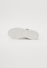 Hvit sneakersåle med teksturert gummi, med sirkulære og diamantmønstre. Designet inkluderer en glatt, avrundet tåområde.