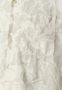 Korte mouw shirt van beige linnen met een bloemmotief, een opgestikte zak en witte knopen voor de sluiting, biedt een lichte textuur.