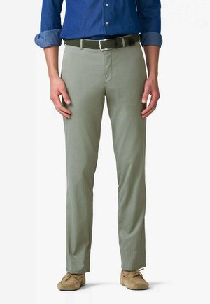 Uomo che indossa pantaloni slim fit grigio chiaro, cintura intrecciata oliva, scarpe casual color cuoio chiaro e camicia blu scuro a maniche lunghe con maniche arrotolate.