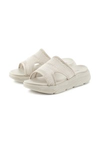 Beige slip-on sandals with woven textile upper, textured midsoles, and cushioned footbeds. Contoured shape for comfort.