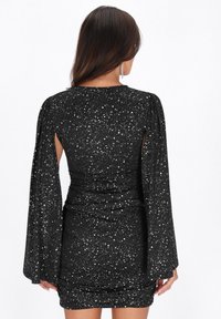 Rochie mini neagră cu un model mânjit în alb, având mâneci lungi și fluide și un design ajustat, strâns în talie.