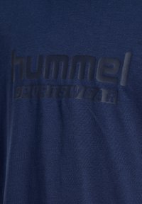 Granatowa koszulka z teksturowanym, czarnym logo "hummel sportswear" na piersi; wykonana z miękkiego materiału bawełnianego o gładkim wykończeniu.