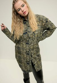 Camicia a maniche lunghe con bottoni caratterizzata da una stampa di serpente verde e nera. Il tessuto ha una texture liscia e una vestibilità comoda.