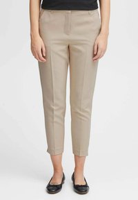Pantaloni beige su misura con una vestibilità slim, dotati di tasche laterali e una piega lungo la parte anteriore. Realizzati in tessuto liscio, con lunghezza cropped.