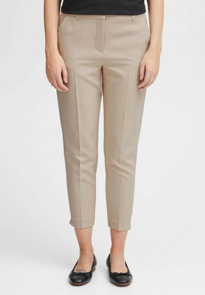 Pantaloni beige su misura con una vestibilità slim, dotati di tasche laterali e una piega lungo la parte anteriore. Realizzati in tessuto liscio, con lunghezza cropped.