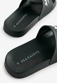 Čierne kĺzavé sandále s textúrovanou podrážkou a hladkým vrchom. Obsahujú logo "ALLSAINTS" v bielej farbe, minimalistický dizajn a tvar na obúvanie.