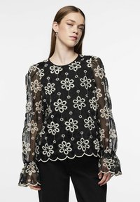Sort bluse med gennemsigtige lange ærmer, der har hvid blomsterbroderi og bølgede kanter. Stoffet har et blødt, tekstureret udseende.