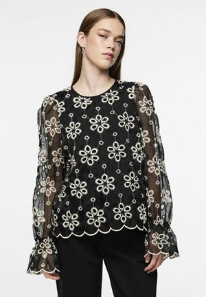 Sort bluse med gennemsigtige lange ærmer, der har hvid blomsterbroderi og bølgede kanter. Stoffet har et blødt, tekstureret udseende.