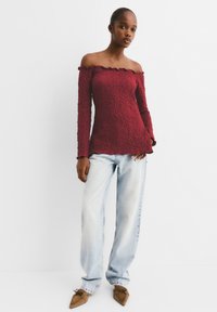 Top lungo a maniche lunghe bordeaux senza spalle in tessuto testurizzato, abbinato a jeans azzurri a vestibilità morbida e scarpe marroni a punta.