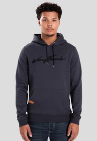 Donkergrijze hoodie met een voorzak, een capuchon met trekkoord en geborduurde "Wrong Friends" letters. Heeft een klein oranje label aan de zijkant.