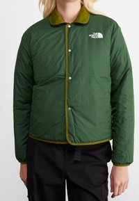 Grön isolerad jacka med en kontrasterande olivfärgad krage och tryckknappsstängning. Har The North Face-logotypen på vänster bröst.