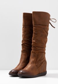 Bottes montantes en cuir marron avec un design froissé, bout arrondi, semelle en caoutchouc et détail de lien en haut ; présente une finition subtilement texturée.