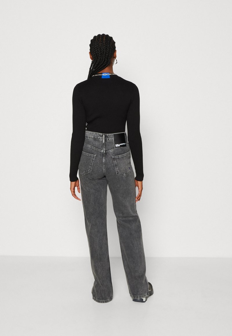 Un haut noir à manches longues côtelé associé à un jean gris taille haute avec une étiquette sur la poche arrière. Le jean a une coupe droite.
