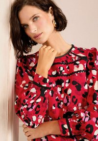 Blusa a maniche lunghe in tessuto rosso con stampa animale multicolore. Presenta rifiniture nere lungo il collo e polsini a sbuffo.