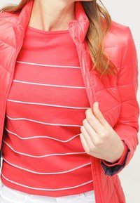 En ljusrosa puffjacka med ståkrage, kombinerad med en röd topp med vita horisontella ränder. Texturerat material och figurnära design.