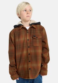 Camicia di flanella a quadri arancione e oliva con bottoni neri, dotata di cappuccio foderato in sherpa e taschino singolo sul petto.